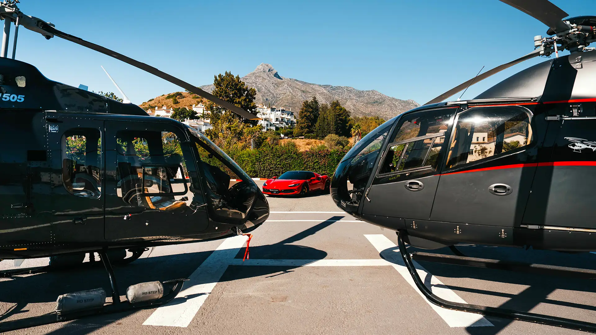 Two black helicopters on a Marbella helipad with the La Concha mountain behind